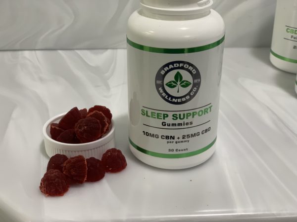 Sleep Support CBD Gummies with the lid off and gummies spread on a white background